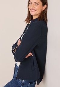 Marine blauwe zip-up jas met een hoge kraag, gemaakt van zachte stof, met zijsplitten en een contrasterende lichtgekleurde voering.