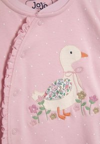 Un capo in cotone rosa presenta pois bianchi, un bordo arricciato e un'anatra ricamata con accenti floreali nella parte inferiore.