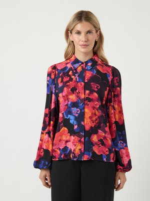 Långärmad blus i svart tyg prydd med livfulla blommönster i rosa, blått och orange; har en krage och puffärmar.