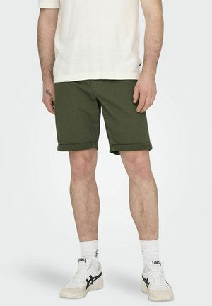 Green cotton shorts with rolled hems, paired with white textured t-shirt and white sneakers featuring black accents. Simple, casual design.