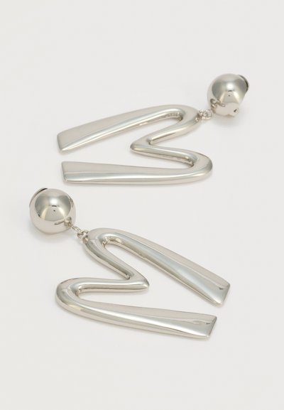 Ασημένια μεταλλικά αφηρημένα σκουλαρίκια σταγόνα ζιγκζαγκ με σφαιρικούς σταυρούς σε λευκό απλό φόντο.