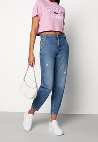 Zkrácený růžový tričko s potištěným textem, modré vysoce pasované džíny s poškozením, bíla taška s řetězem a bílé tenisky s tlustou podrážkou.