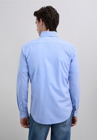 Cămașă bleu cu mâneci lungi, cu guler cu nasturi, textură netedă, cusătură pe spate și manșete cu nasturi. Purtați cu blugi casual de denim.