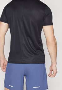 Svart tränings t-shirt gjord av lätt, slät tyg med korta ärmar, centrerad söm på ryggen, i kombination med blå shorts med vita detaljer.