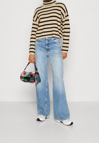 Un col roulé rayé beige et noir, un jean taille haute bleu clair à jambes larges, et un sac à main à motifs colorés avec une poignée noire. Des baskets blanches sont portées.