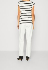 Top de rayas negras y blancas con mangas cortas, combinado con pantalones rectos blancos y zapatos de tacón negros. Tejido suave, diseño simple.
