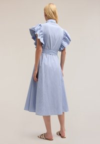 Rochie albastru deschis cu dungi, cu mâneci bufante din voal, talie cu curea și fustă fluidă, confecționată dintr-un material ușor. Design minimalist.