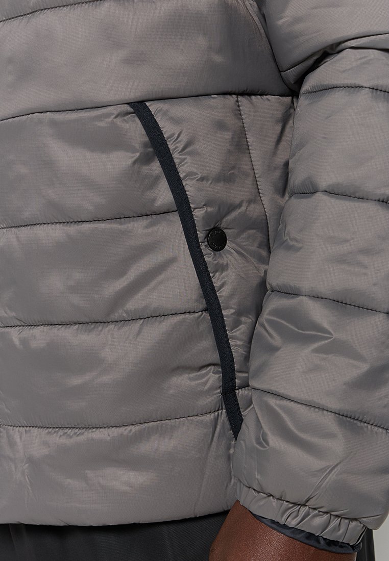 Giacca a vento grigia con design trapuntato, polsini elasticizzati e bordatura blu marina lungo la tasca con cerniera; texture liscia con finitura lucida.
