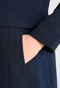 Abito blu navy con un design pulito, tessuto strutturato, una tasca laterale e una vestibilità su misura con una finitura liscia.