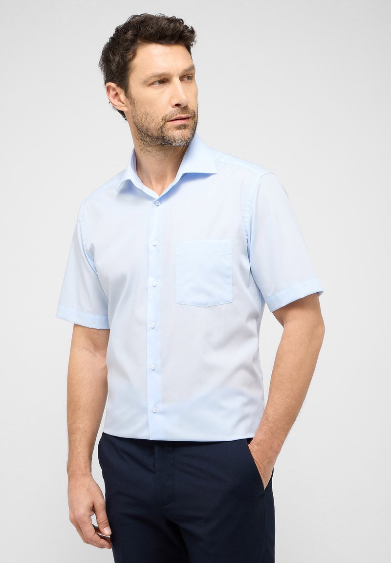 Lichtblauw kortarmshirt met een klassieke kraag, knopen aan de voorkant en een linkse borstzak. Soepele stof met een lichte glans.