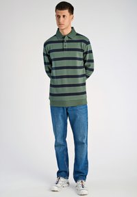 Zielona koszulka polo w paski z granatowymi poziomymi pasami, z trzema guzikami, zestawiona z niebieskimi dżinsami i białymi trampkami.