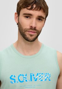 Hellgrünes ärmelloses Tanktop mit einem auffälligen blauen und gemusterten "S.OLIVER"-Logo. Weicher Stoff mit lockerer Passform und rundem Ausschnitt.