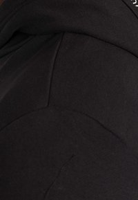 Tessuto nero con una texture liscia, caratterizzato da un design contemporaneo e cuciture strutturate, che mostrano dettagli di cucitura sottili.