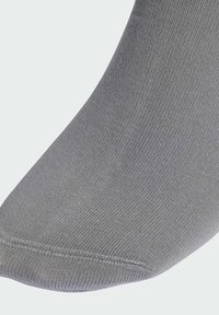 Šedá ponožka s hladkou texturou, žebrovaným designem a kulatou špičkou. Materiál působí lehce a elasticky. Nejsou viditelné žádné vzory ani dekorace.