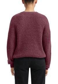 Pull en tricot bordeaux avec une coupe texturée et ample, doté de manches longues et d'un col rond. Porté avec un pantalon noir, vue de dos.