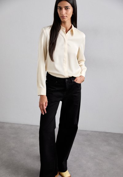Cream button-up shirt with long sleeves, paired with high-waisted black wide-leg jeans. The outfit features a relaxed fit and smooth texture.