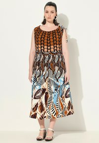 Robe marron et à motifs avec un haut ajusté, des bretelles nouées sur les épaules et une jupe fluide ornée de motifs en feuilles et géométriques dans des tons de bleu, marron et crème.