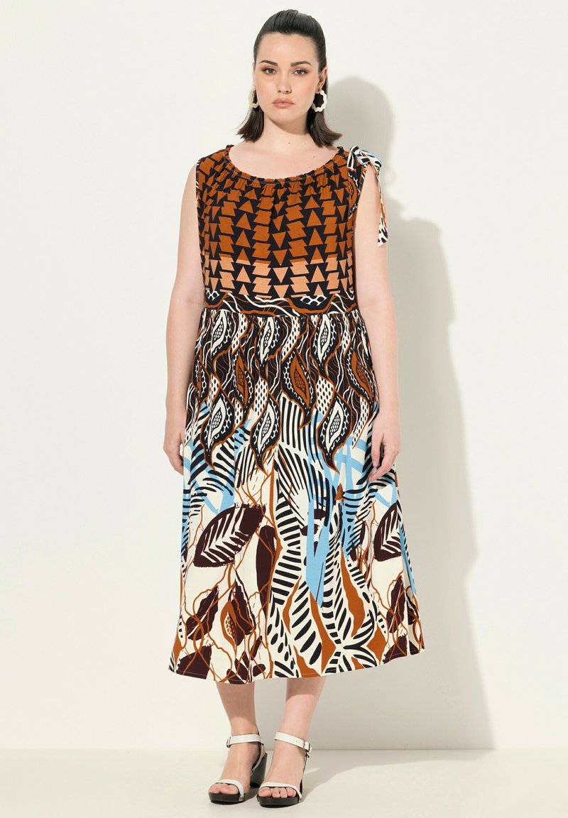 Robe marron et à motifs avec un haut ajusté, des bretelles nouées sur les épaules et une jupe fluide ornée de motifs en feuilles et géométriques dans des tons de bleu, marron et crème.