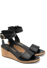 Czarne skórzane sandały na koturnie z paskami wokół kostki, teksturowane plecione podeszwy, gładkie wkładki oraz akcenty w kolorze złotym.