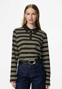 Rudas ilgomis rankovėmis polo marškinėliai su žaliai baltomis juostelėmis, tamsia apykakle ir trijų mygtukų pločiu, derinami su aukštakulnėmis džinsinėmis kelnėmis.