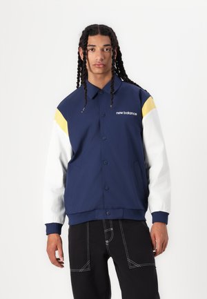 Veste bleu marine avec des manches blanches et jaunes ; comporte des boutons, un col et des poches latérales ; fabriquée dans un tissu lisse et texturé.