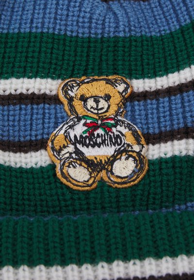Adīta cepure ar horizontālām svītrām zaļā, zilā un baltā krāsā; rotāta ar izšūtu lāci, kurš uzvelk kreklu ar "Moschino" logo.