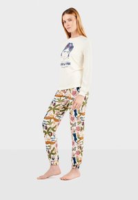 Set van damespyjama's met een crème kleurige langarmtop met een graphic en kleurrijke, patroonachtige broek met bloemen- en dierenmotieven.