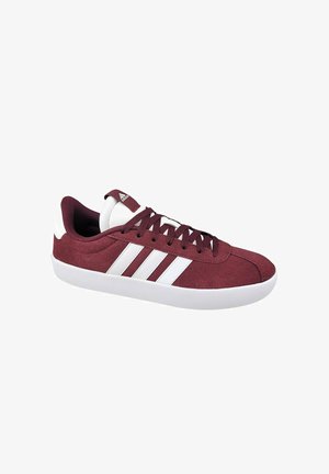 Burgundy suede sneaker with white accents, featuring a rounded toe, flat sole, and lace-up design. Three white stripes on the side.