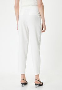 Witte, op maat gemaakte broeken met een slim fit, voorzien van achterzakken, een zachte textuur en een medium taille. Gecombineerd met zwarte strappy hakken.