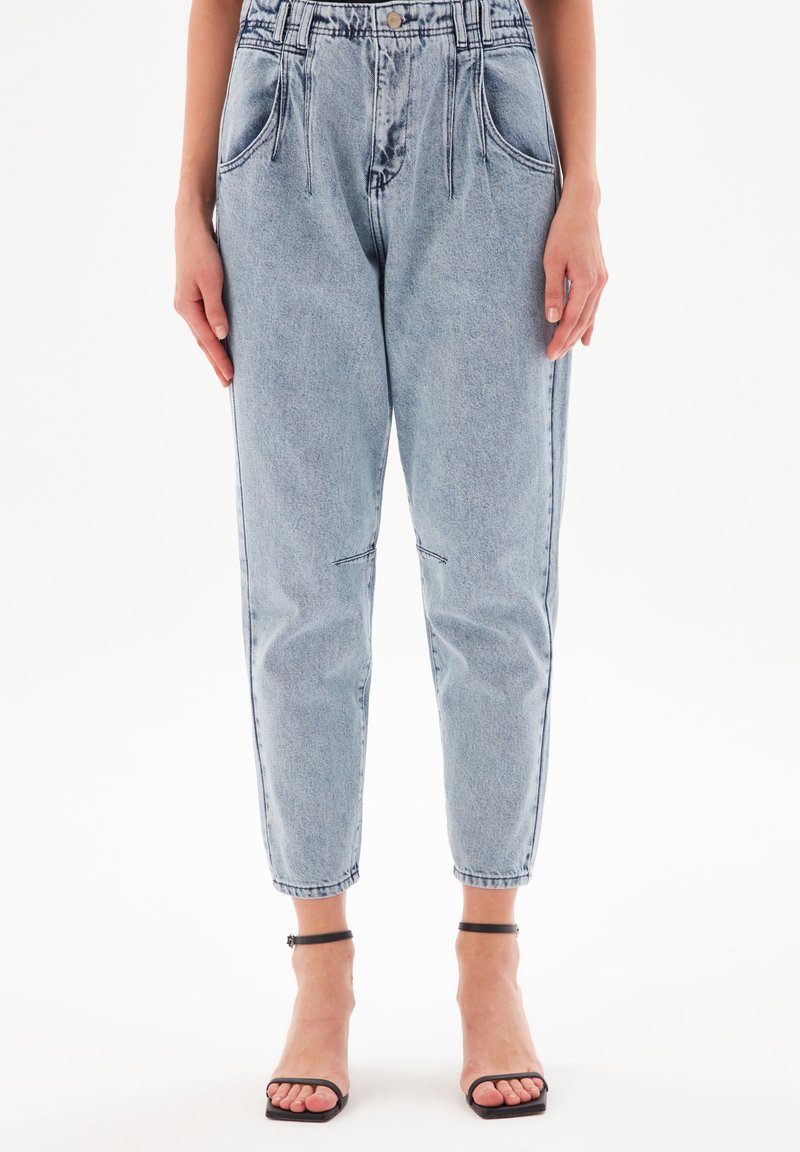 Světle modré džínové kalhoty s vysokým pasem, zúženými nohavicemi, předními sklady a bočními kapsami. Dokončeno zipem a zapínáním na knoflík.