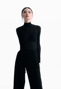 Svart langermet bodysuit med høy hals og tettsittende design, kombinert med høytlivede svarte bukser. Klare hoopear som tilbehør.