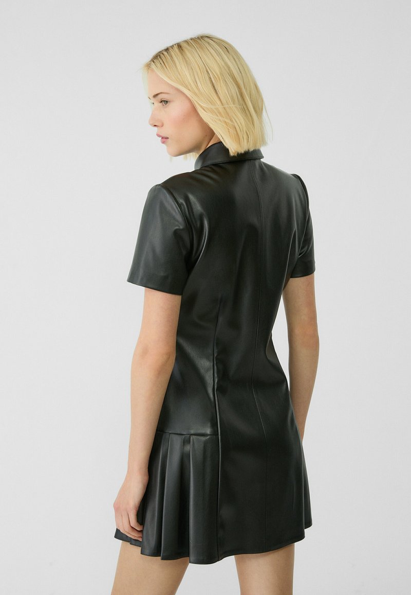 Abito in pelle nera con maniche corte e gonna plissettata. Presenta un corpetto aderente e un colletto alto, mettendo in mostra una texture elegante.