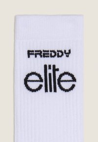 Calcetín blanco de canalé con el nombre de la marca "FREDDY" en texto negro encima de "elite" en una fuente negra más grande, con un diseño redondeado.