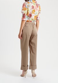 Blusa floreale con maniche a sbuffo in colori pastello, abbinata a pantaloni beige a vita alta e a gamba affusolata con orli a risvolto e una cintura elasticizzata.