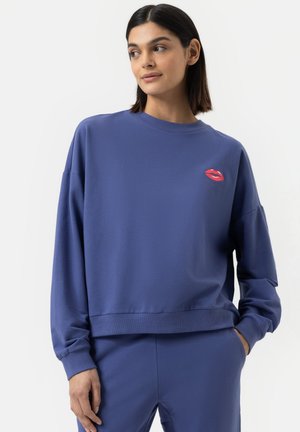 Lila Sweatshirt mit Rundhalsausschnitt und tiefen Schultern. Mit einer roten Lippenstickerei auf der linken Brust. Weicher Stoff.