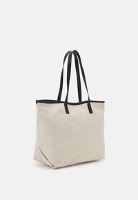 Canvas tas in lichtbeige met zwarte leren afwerking en hengsels. Vierkante vorm, zachte textuur en een open ontwerp zonder extra details.