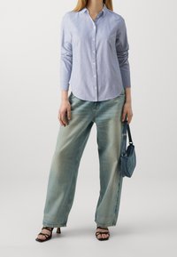 Blue and white striped button-up shirt, full sleeves, paired with light blue wide-leg jeans and black strappy sandals, holding a small denim bag.