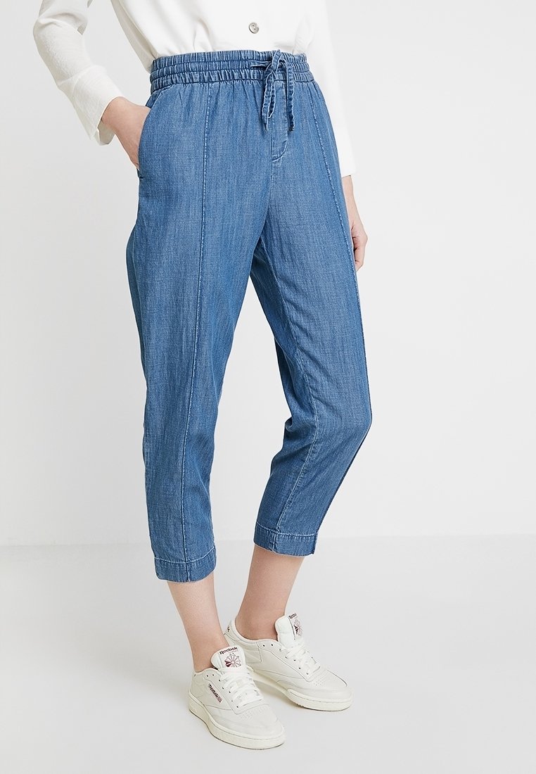 Pantalon en denim bleu clair avec une taille élastique et un cordon de serrage, doté de poches latérales et d'une coupe courte. Porté avec des baskets blanches.