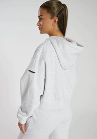 Felpa oversize grigia chiara in morbido tessuto, con cappuccio, maniche ampie, polsini a costine e un piccolo logo nero sulla manica sinistra.