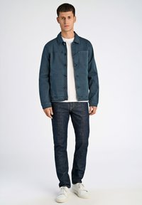 Sininen farkkutakki napin kiinnityksellä, rintatasku, valkoisen t-paidan päällä. Yhdistetty tummiin farkkuihin ja valkoisiin tennareihin.