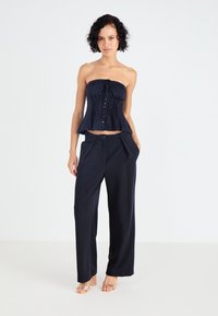 Ναυτικό strapless peplum τοπ με λεπτομέρεια κουμπιού, συνδυασμένο με χαλαρές ναυτικές παντελόνες. Λείος υφασμάτινος υφής, μινιμαλιστικός σχεδιασμός και χωρίς σχέδια.