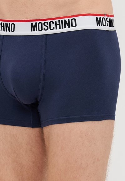 Σκούρο μπλε βαμβακερά μποξεράκια με λευκή ζώνη που έχει μαύρη επιγραφή "MOSCHINO" και κόκκινες λεπτομέρειες; λείο υλικό, στενή εφαρμογή.