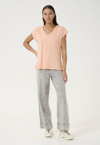 T-shirt V à col en pêche avec des manches capes, associé à un jean large gris clair. La tenue présente une coupe décontractée et une texture douce.