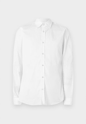 Biela košeľa s dlhým rukávom na gombíky, vyrobená z bavlny. Má špicatý golier a malú vyšívanú logo na hrudi. Hladká textúra.