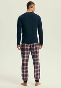 Granatowy top z długim rękawem zestawiony z kraciastymi piżamowymi spodniami w kolorach czerwonym, granatowym i białym. Spodnie mają elastyczne mankiety i wygodne dopasowanie.