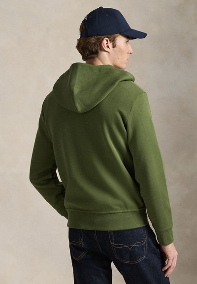 Πράσινη βαμβακερή φούτερ με κουκούλα και κορδόνι, ριμπ μανσέτες και τελείωμα, σε συνδυασμό με σκούρο τζιν παντελόνι. Η πίσω όψη δείχνει απλό σχέδιο και σιλουέτα.