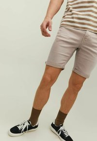 Pantalones cortos de mezclilla beige claro con puños enrollados, combinados con zapatillas negras y calcetines marrones. La parte superior presenta rayas horizontales beige y blancas.