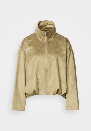 Veste beige en suédine avec fermeture éclair, col montant, manches longues et taille légèrement froncée, présentée sur un fond uni.