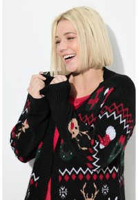 Schwarze Strickjacke mit roten, grünen und weißen Feiertagsmotiven, darunter Rentiere und Schneeflocken. Mit gerippten Bündchen und Kragen.