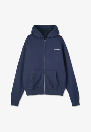 Navy blue zip-up hoodie featuring a hood, front pockets, ribbed cuffs, and a small "PEGADOR" logo on the left chest. Soft material texture.